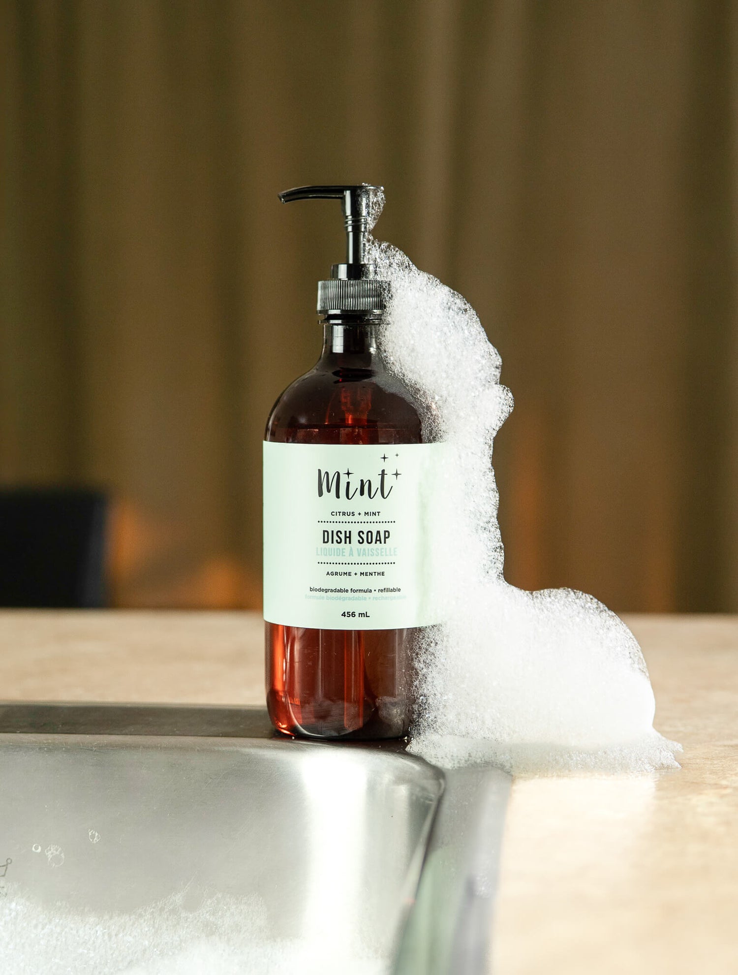 Bottle of dish soap with a pump dispenser on a sink, labeled 'Mint'.