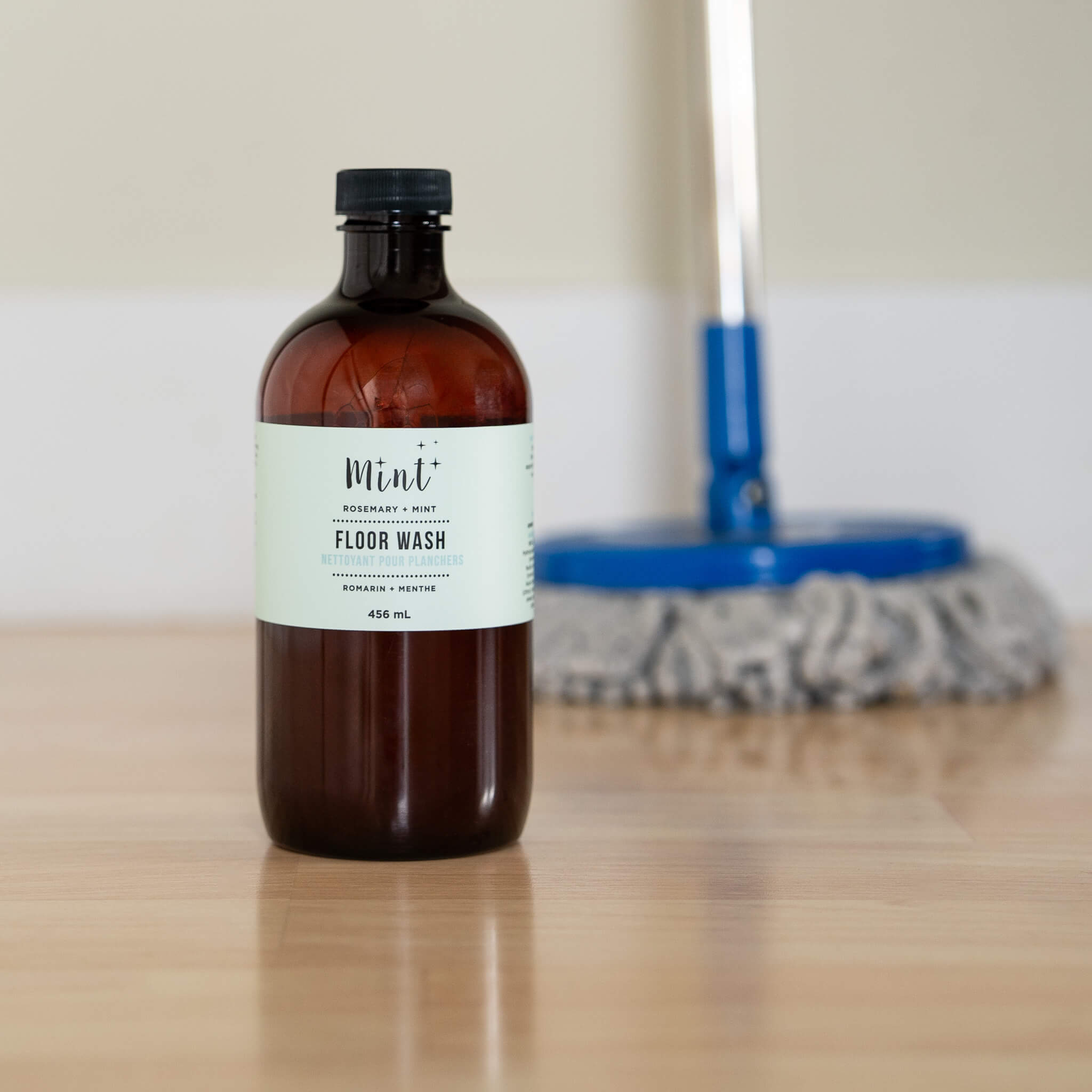 Bottle of Mint Floor Wash on a wooden surface with cleaning tools in the background