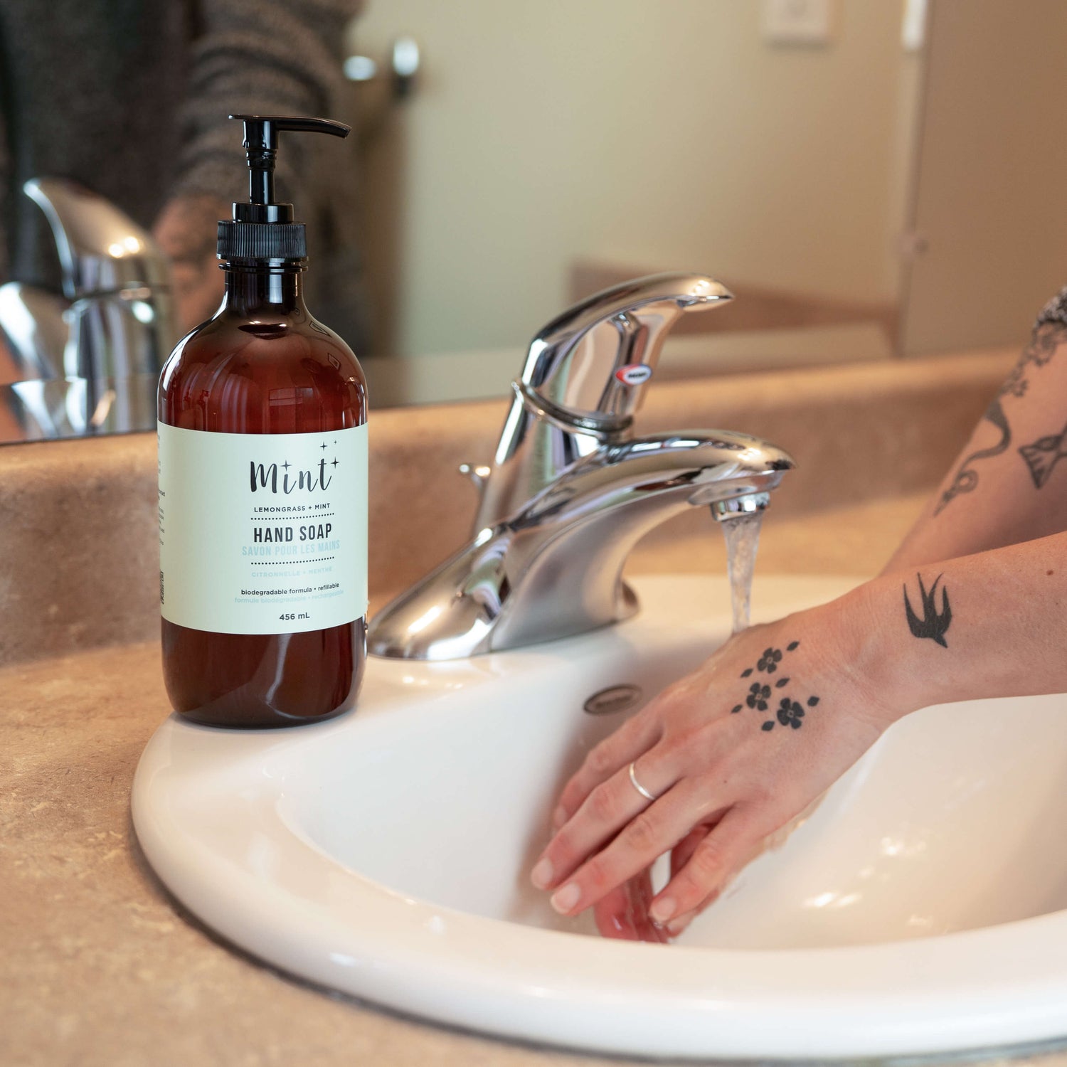 Hand soap bottle labeled 'Mint' on a sink with a person washing hands.