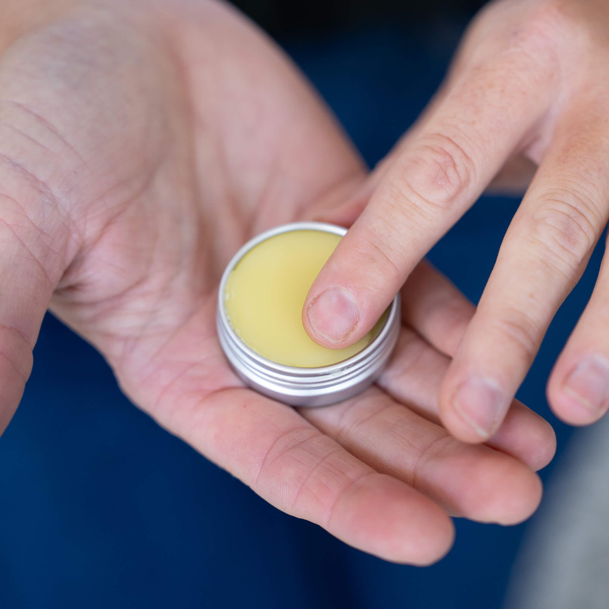Close-up of hand holding an open tin of Mint Vanilla + Mint Lip Salve with balm visible