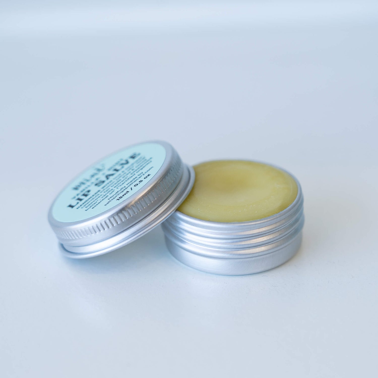 Open and closed tins of Mint Vanilla + Mint Lip Salve showing creamy balm inside.