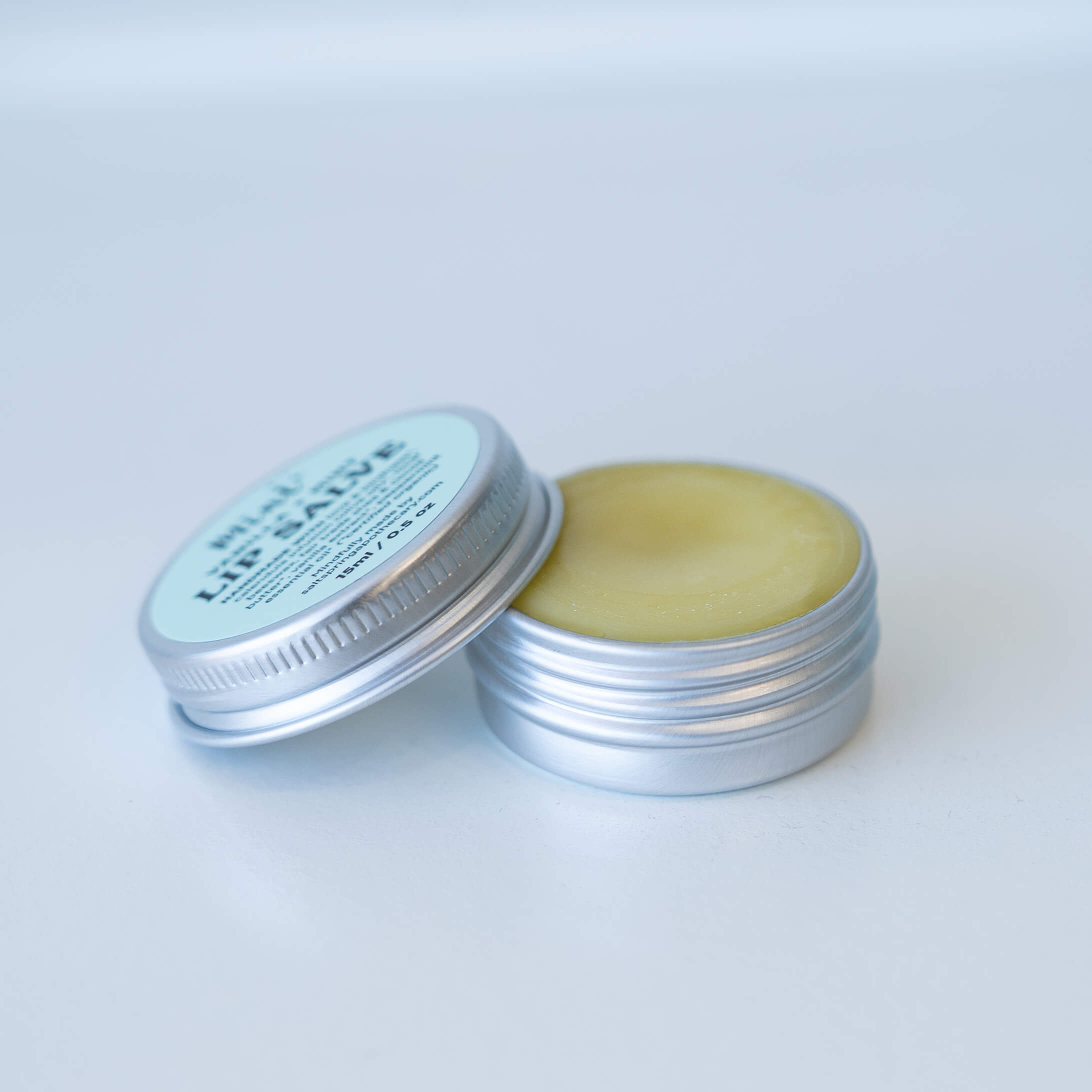 Open and closed tins of Mint Vanilla + Mint Lip Salve showing creamy balm inside.