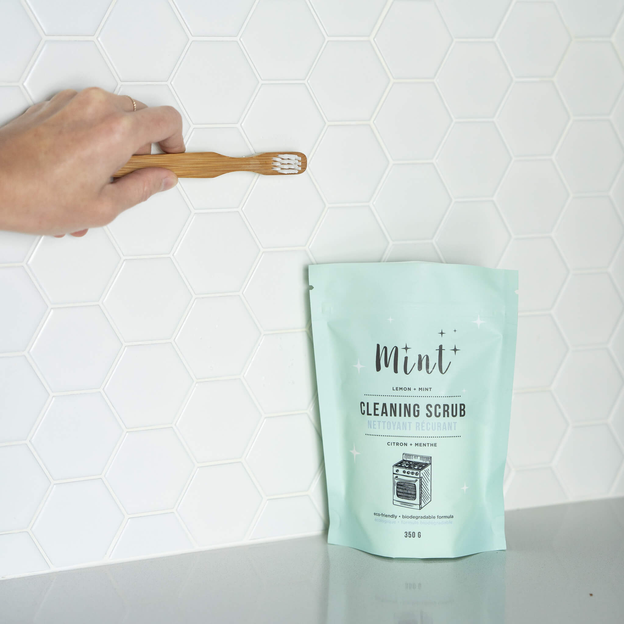 Mint-colored cleaning scrub package with a wooden scrubber on a white tiled background