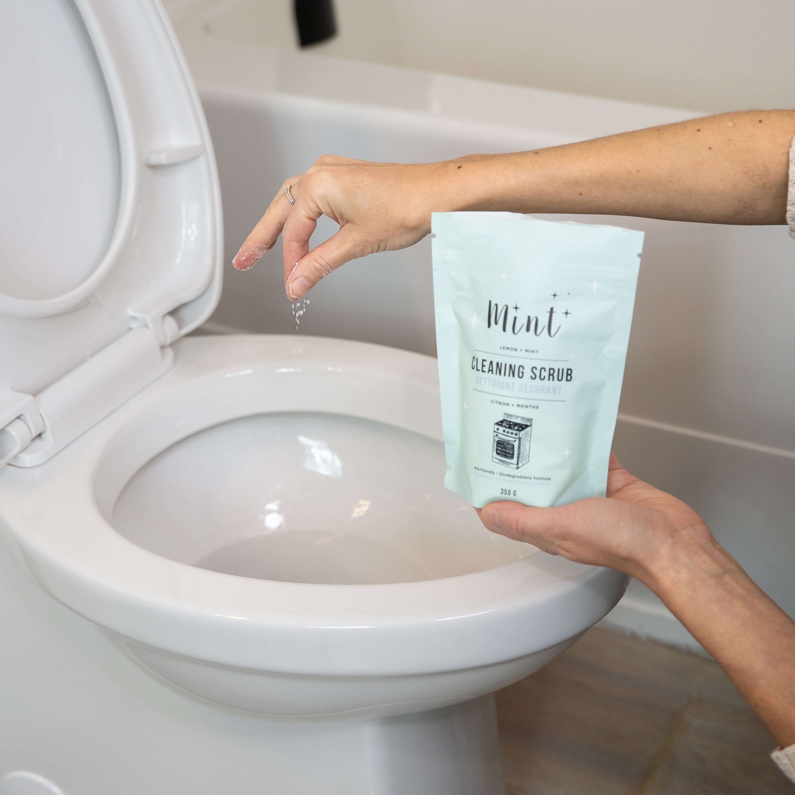 Person holding a bag of cleaning scrub and sprinkling in toilet