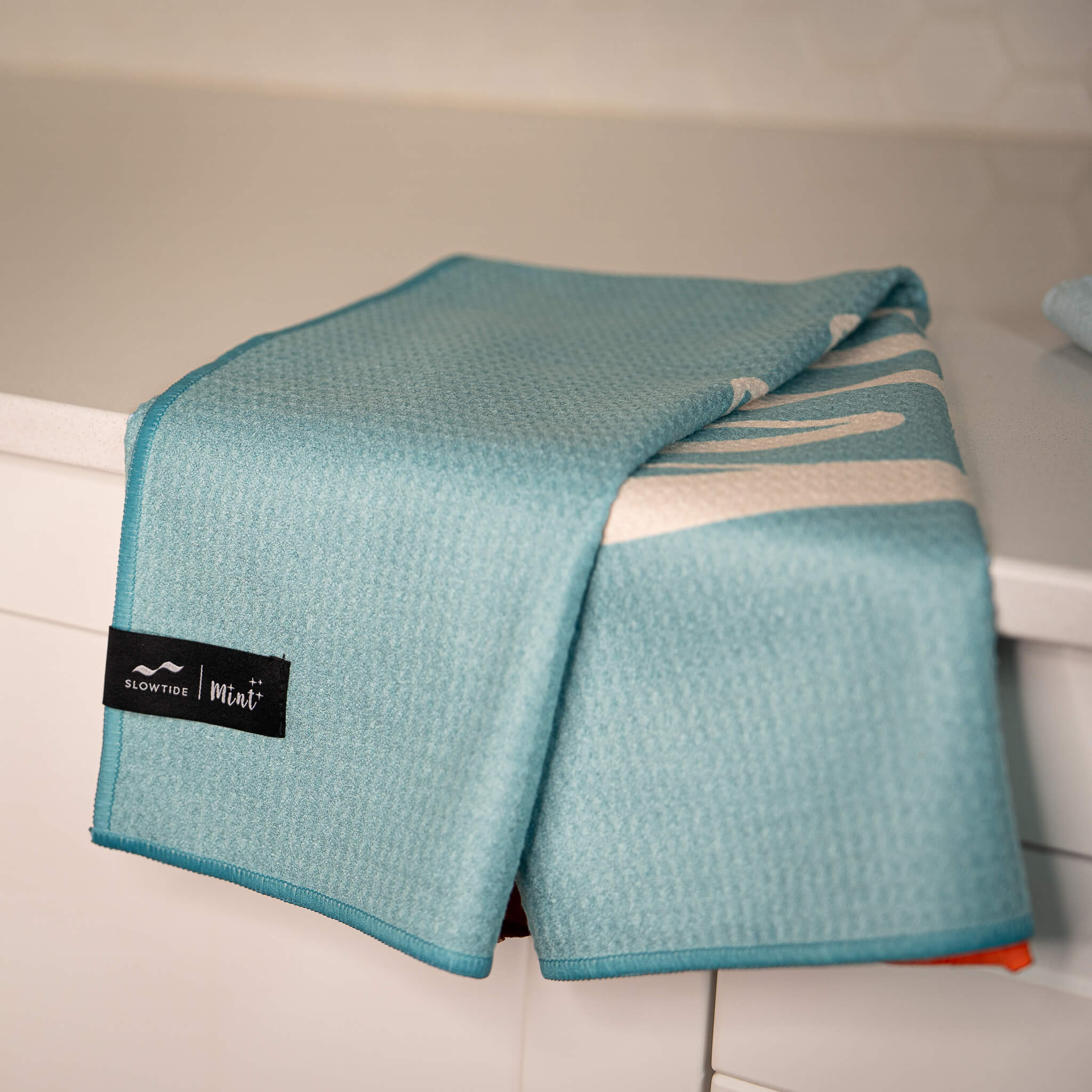 Teal towel with a brand label on a white surface