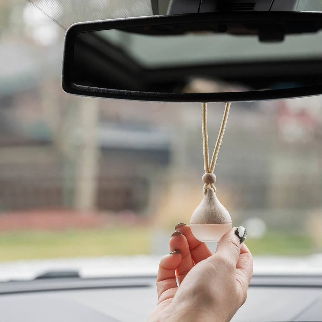 Hand holding a car air freshener against a blurred car interior background