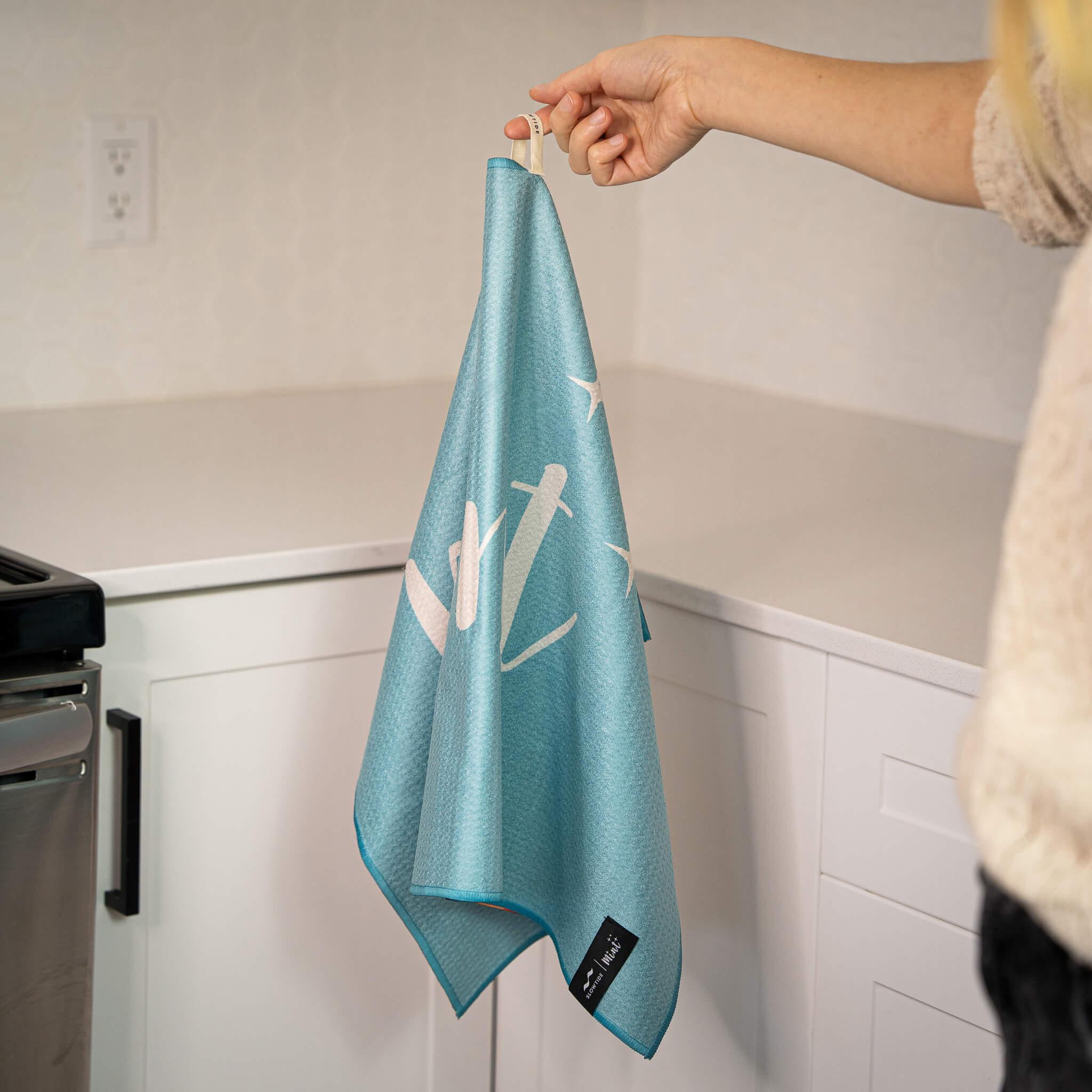 Person holding a blue towel with white designs in a kitchen setting