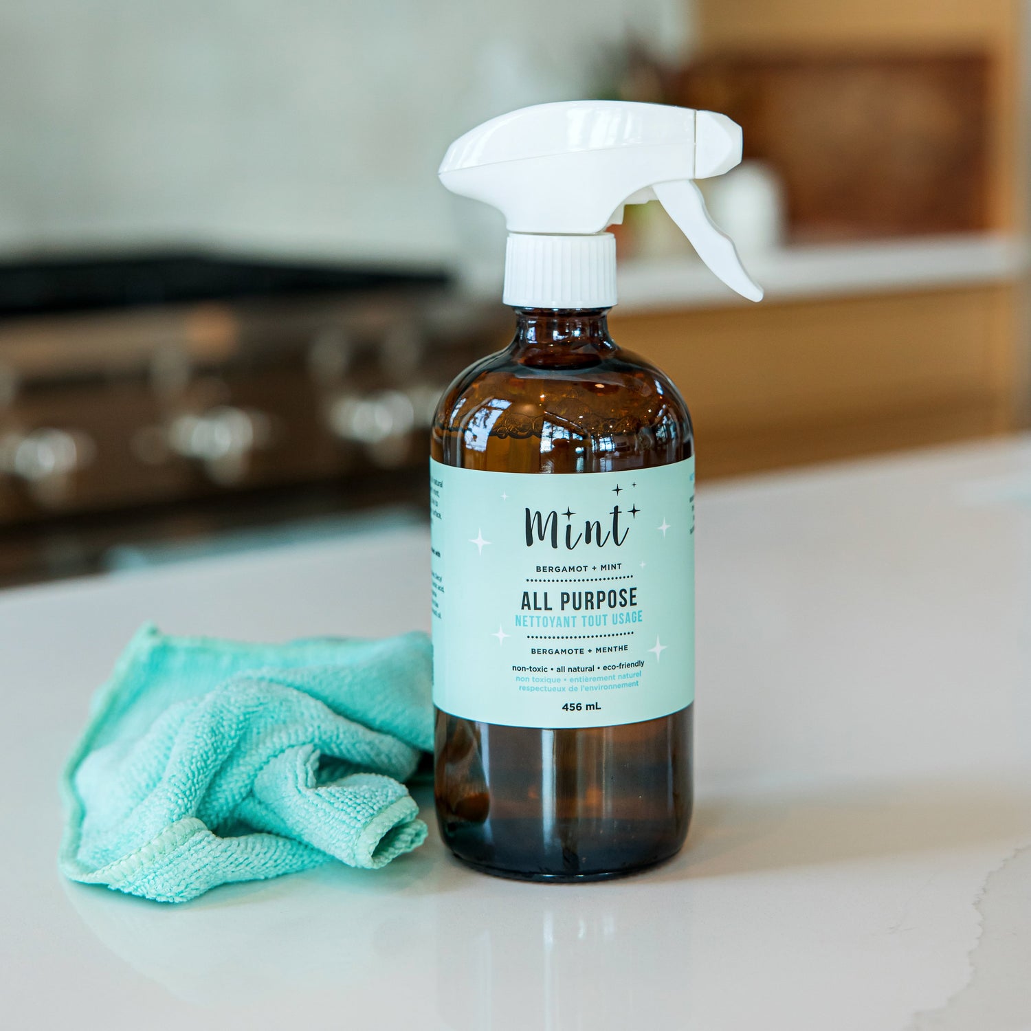 Mint All Purpose Cleaner in a glass spray bottle on a kitchen countertop beside a green cleaning cloth, showcasing a sustainable cleaning setup.