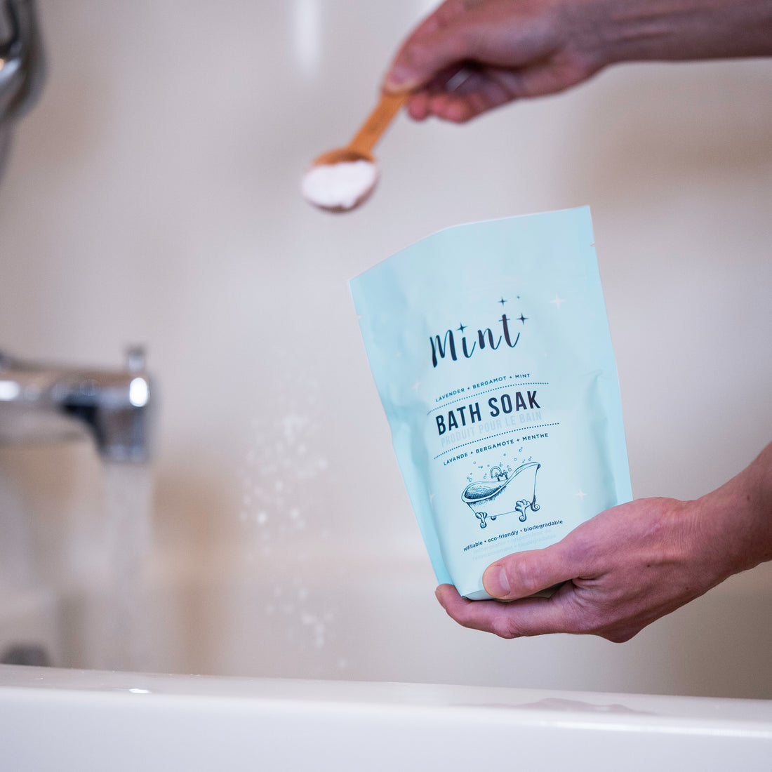 Person sprinkling Mint Bath Soak into a bathtub, demonstrating the ease of use for a soothing, aromatic bath.