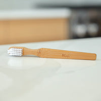 Mint-branded bamboo cleaning brush with white bristles, placed on a clean white surface, emphasizing its natural, eco-friendly design.