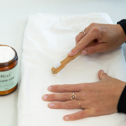 Person using a bamboo cleaning brush to scrub a white fabric surface with Mint&