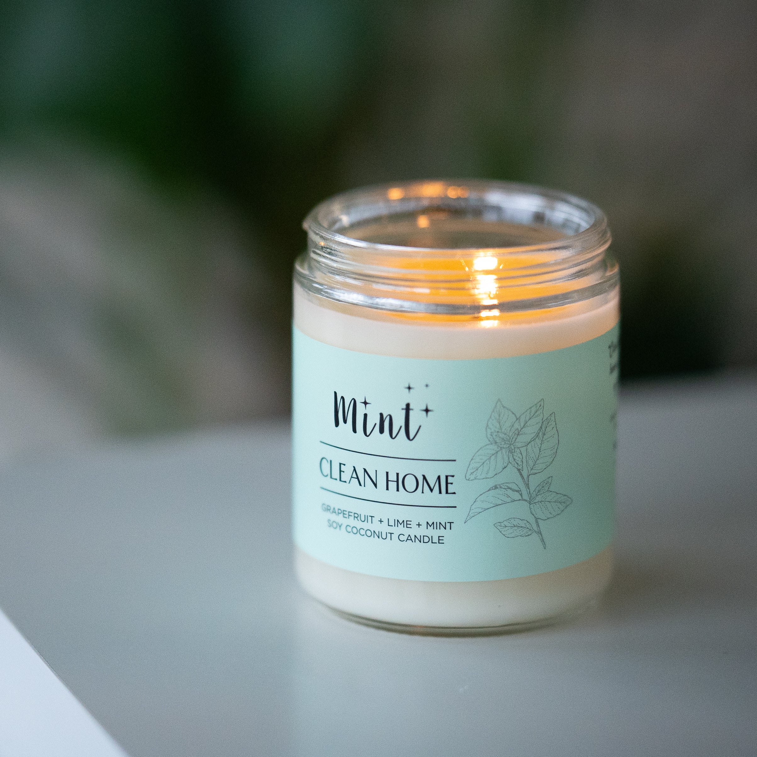 Mint Clean Home soy coconut candle with grapefruit, lime, and mint scent, lit and placed on a table, creating a warm and inviting ambiance.