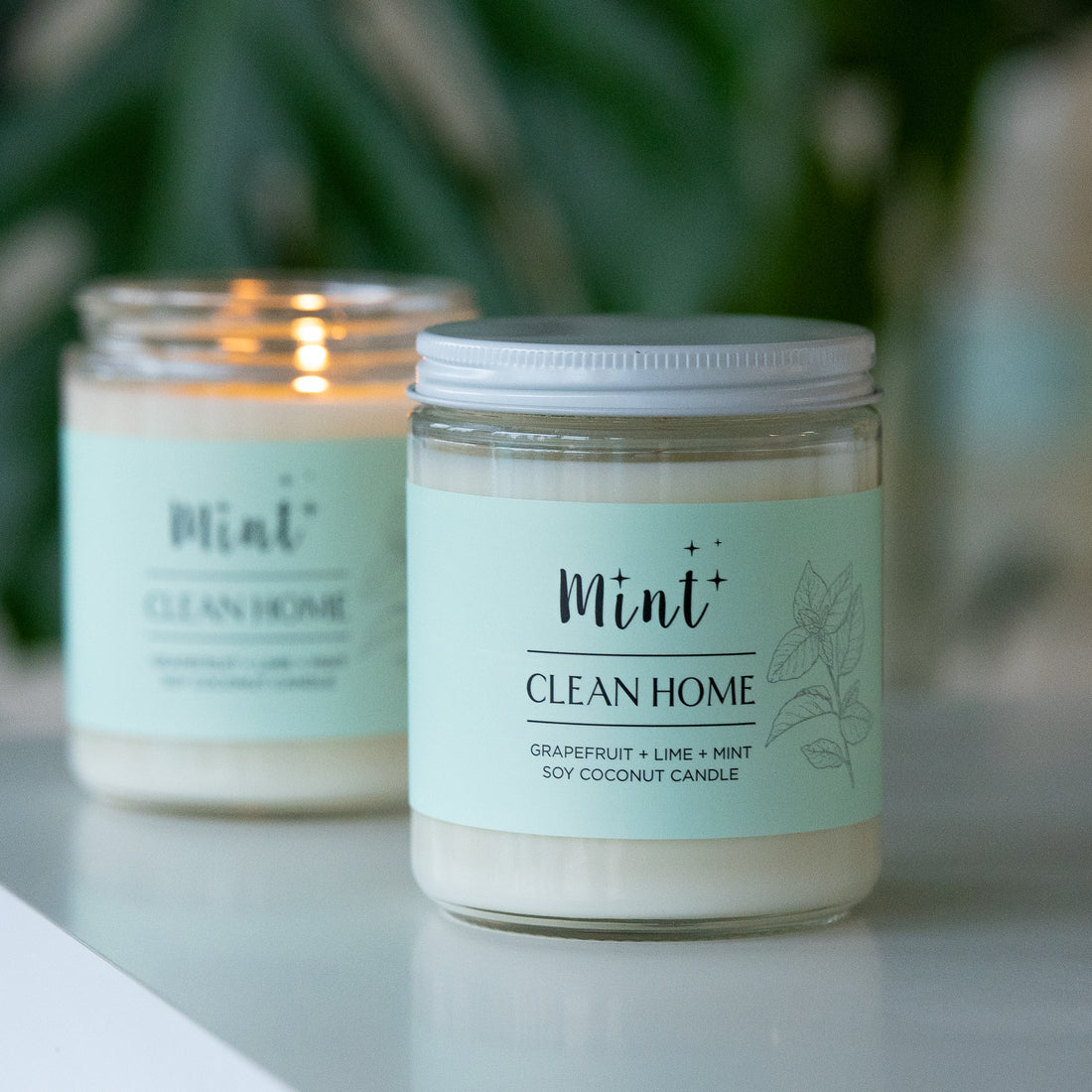 Mint Clean Home soy coconut candle with grapefruit, lime, and mint scent, shown on a table. The jar candle is unlit, and another identical candle is lit in the background.