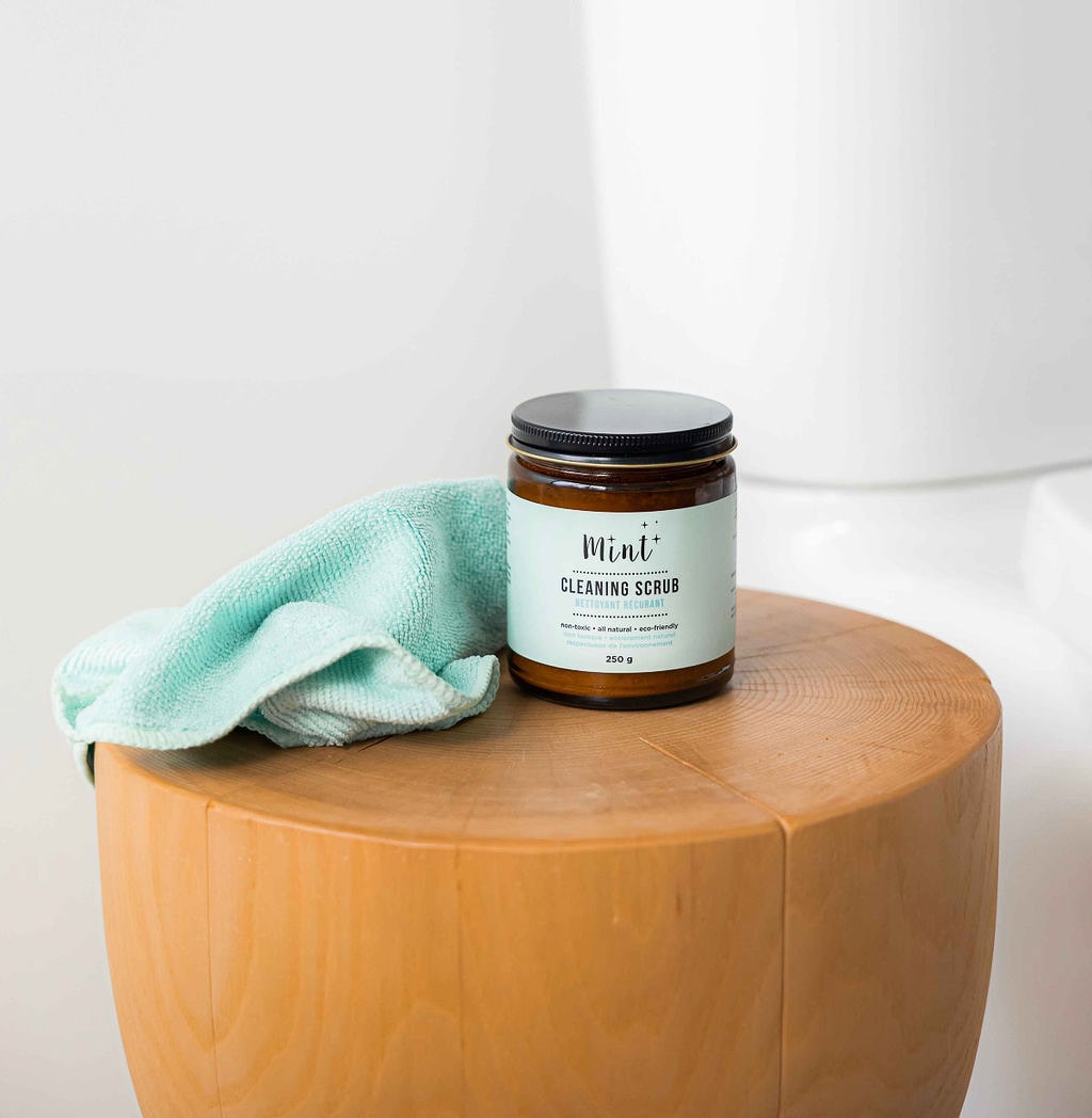 Mint Cleaning Scrub jar on a wooden stool with a microfibre cloth, ideal for versatile, eco-friendly cleaning in any room.