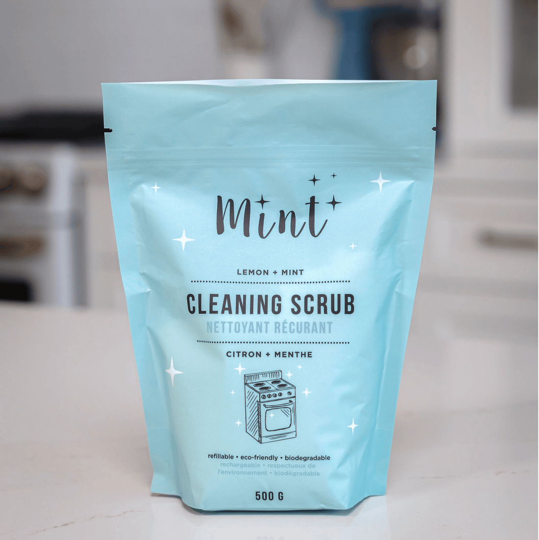 Mint Cleaning Scrub refill pouch (500g) with Lemon + Mint scent, placed on a kitchen counter. The pouch is designed for easy refilling and features labels indicating its eco-friendly and biodegradable nature.