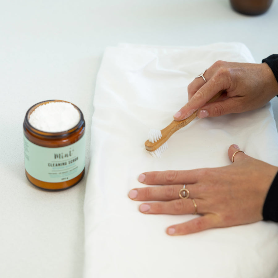 Mint Cleaning Scrub being applied to fabric with a bamboo brush, showcasing its stain-removing power for tough grime.