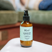 Mint Cleansing Mist bottle displayed on a table in a cozy room, ideal for naturally freshening up linens and spaces.