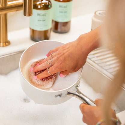 Person scrubbing a stainless steel pot with a Mint copper scrubby, showcasing its effectiveness in removing grime from cookware.