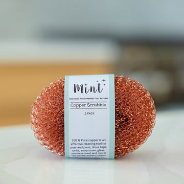 Mint copper scrubby with product label displayed on a kitchen countertop, highlighting 100% pure copper material for effective cleaning.