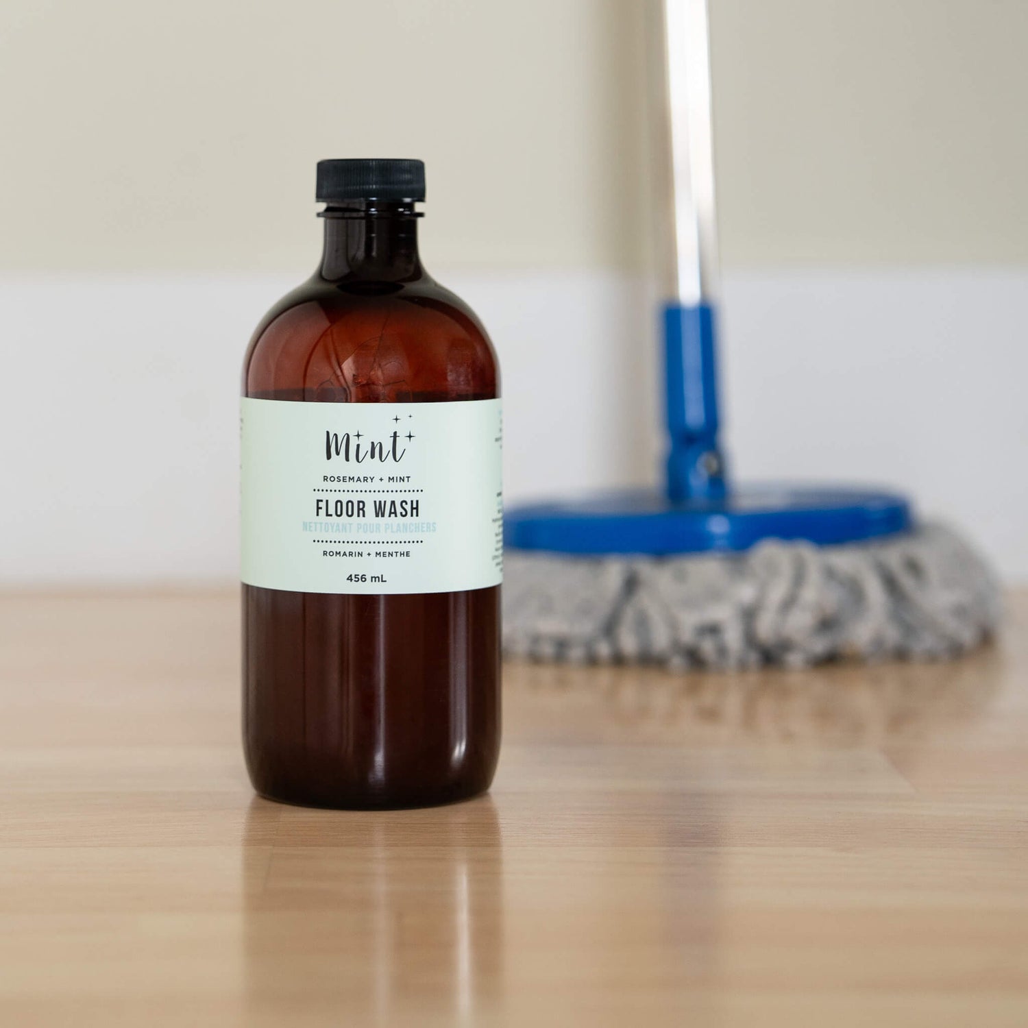 Bottle of Mint Floor Wash on a wooden surface with cleaning tools in the background