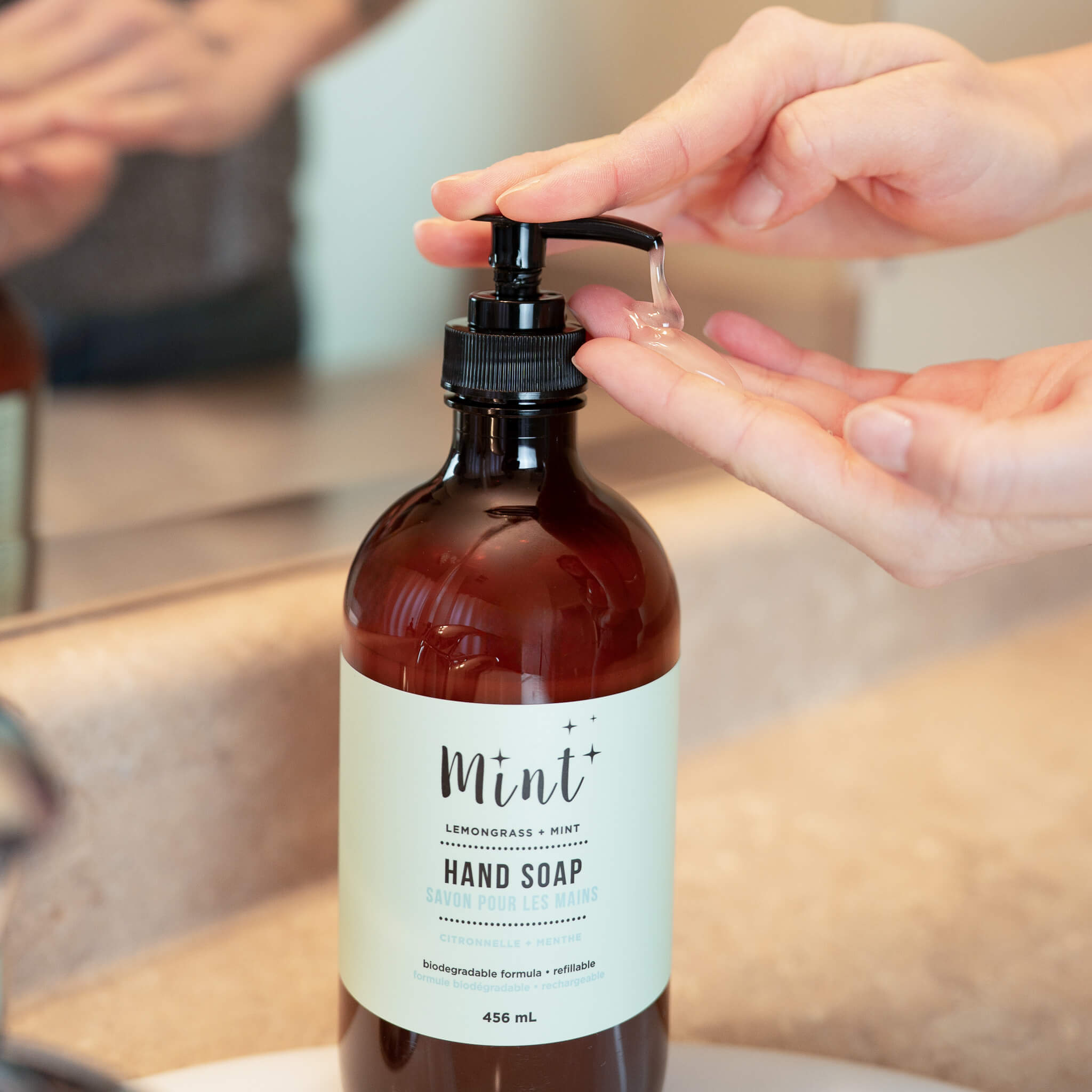 Hand soap bottle with pump being used, labeled &
