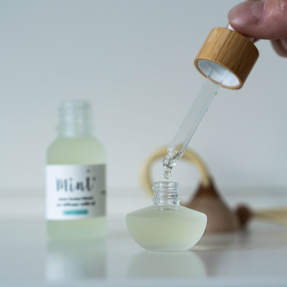 Glass dropper bottle with wooden cap being used to extract liquid from a smaller bottle labeled &
