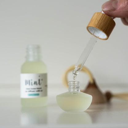 Glass dropper bottle with a wooden cap being used to extract liquid from another bottle labeled &