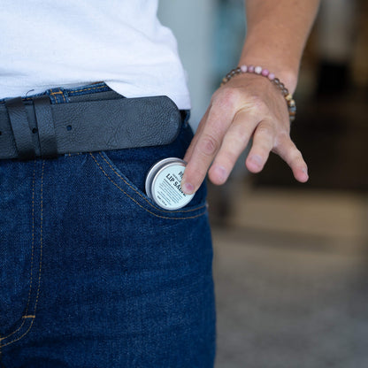 Person placing Mint Vanilla + Mint Lip Salve tin into front pocket of blue jeans.