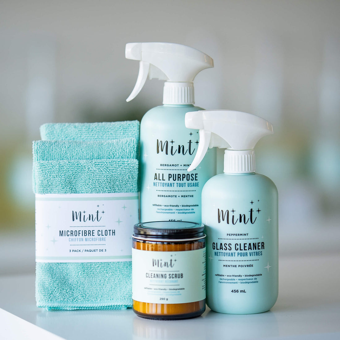 The Essential Home Care Bundle by Mint Cleaning Products, featuring all-purpose cleaner, glass cleaner, cleaning scrub, and a set of microfiber cloths, displayed on a clean surface.