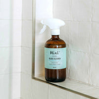 A Mint glass cleaner bottle, placed on a tiled shower shelf, showcasing its sleek design and eco-friendly packaging.