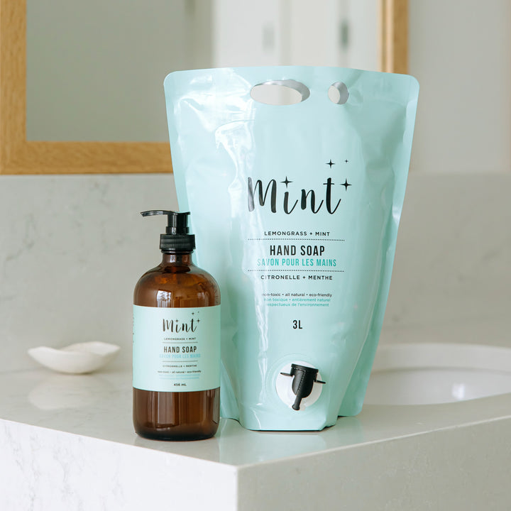 Mint Lemongrass & Mint Hand Soap in a 3L refill pouch with a spout, prominently displayed next to a 456ml glass bottle with a pump dispenser, on a bathroom counter. The pouch label highlights the natural and eco-friendly ingredients.