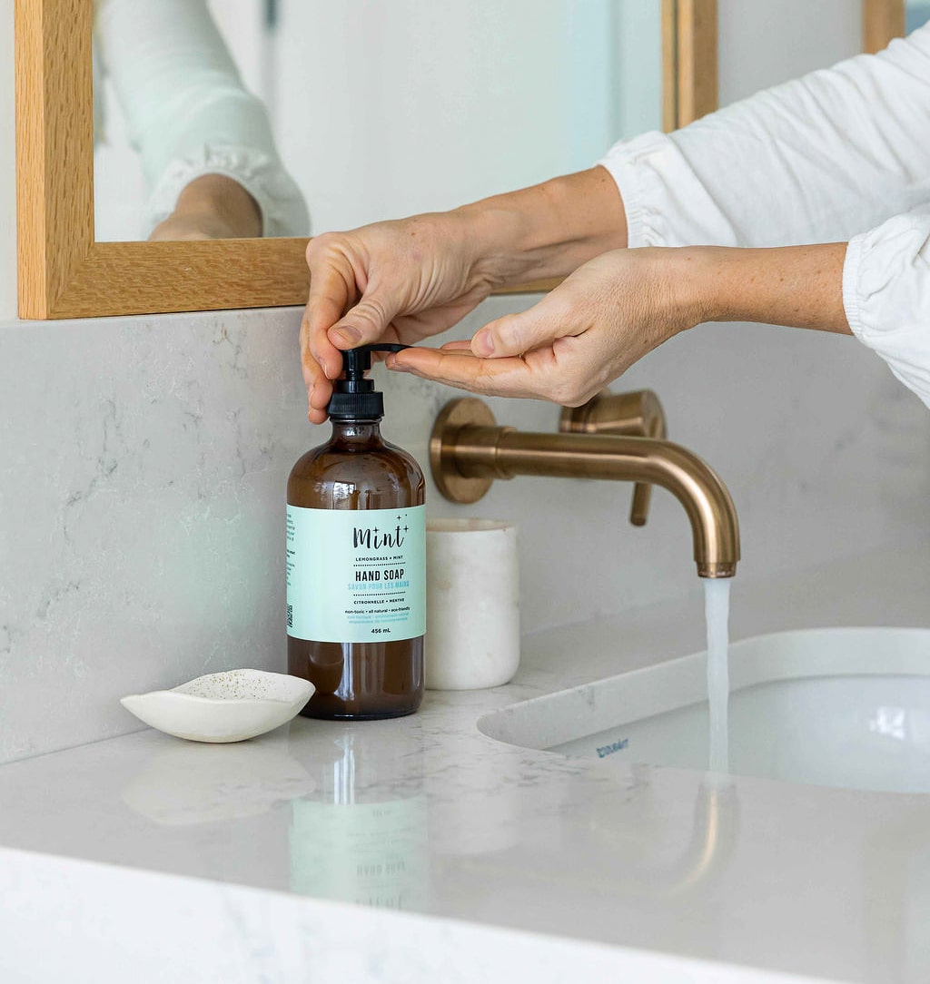 Close-up of Mint Hand Soap being dispensed onto hands at a bathroom sink, showcasing its natural and eco-friendly formula.