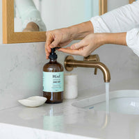 Close-up of Mint Hand Soap being dispensed onto hands at a bathroom sink, showcasing its natural and eco-friendly formula.