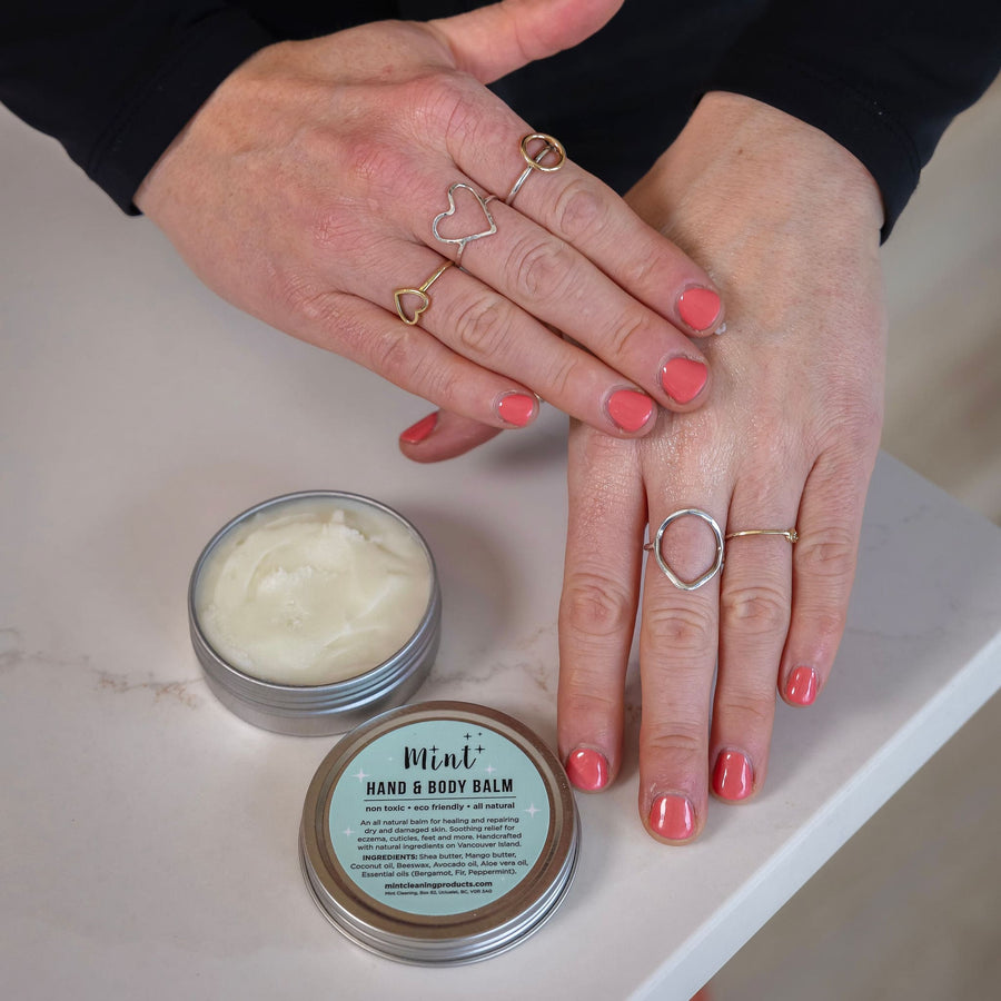 Close-up of hands applying Mint Hand & Body Balm, showing the balm's rich texture and soothing consistency. The tin's label highlights the balm's natural ingredients and eco-friendly formulation.