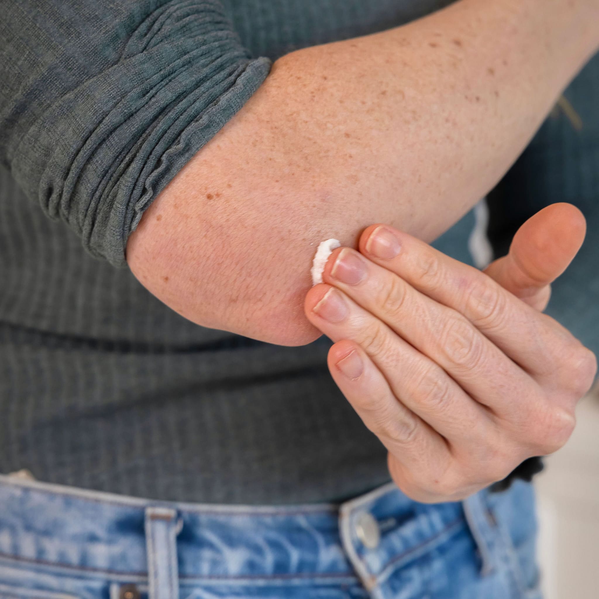 Hand applying a small amount of Mint Hand &amp; Body Balm to an elbow, emphasizing the balm&