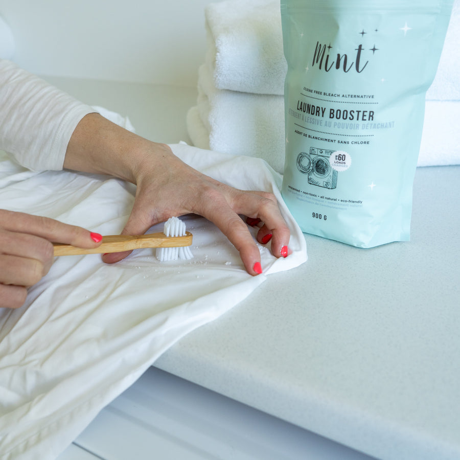 Mint Laundry Booster being applied on a white fabric using a bamboo brush, demonstrating its stain-fighting power and versatility.