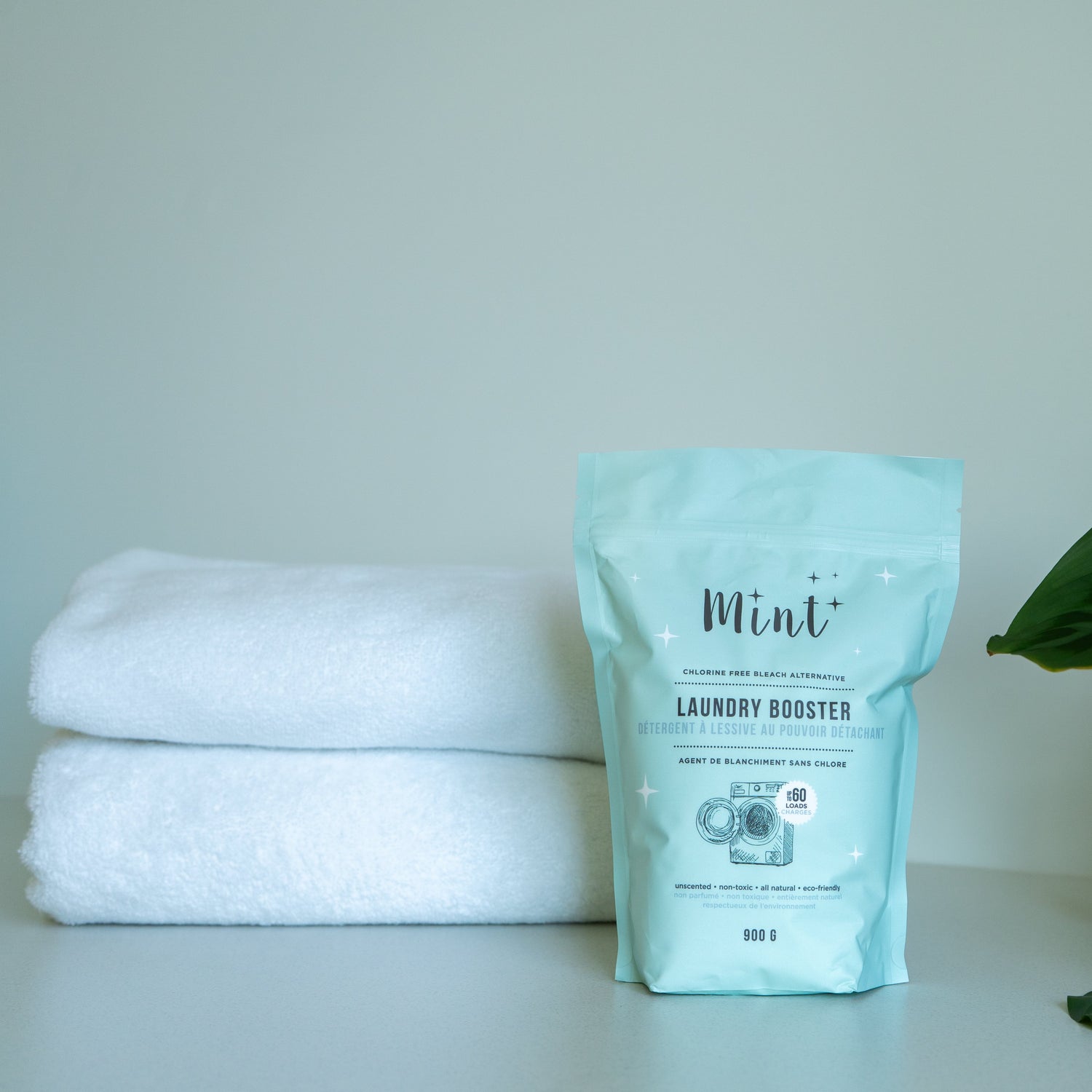 Mint Laundry Booster pouch displayed with clean white towels and a green plant, showcasing its natural and eco-friendly qualities.