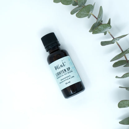 Mint Lighten Up essential oil bottle lying on a white surface with eucalyptus leaves arranged around it, adding a fresh and natural touch.