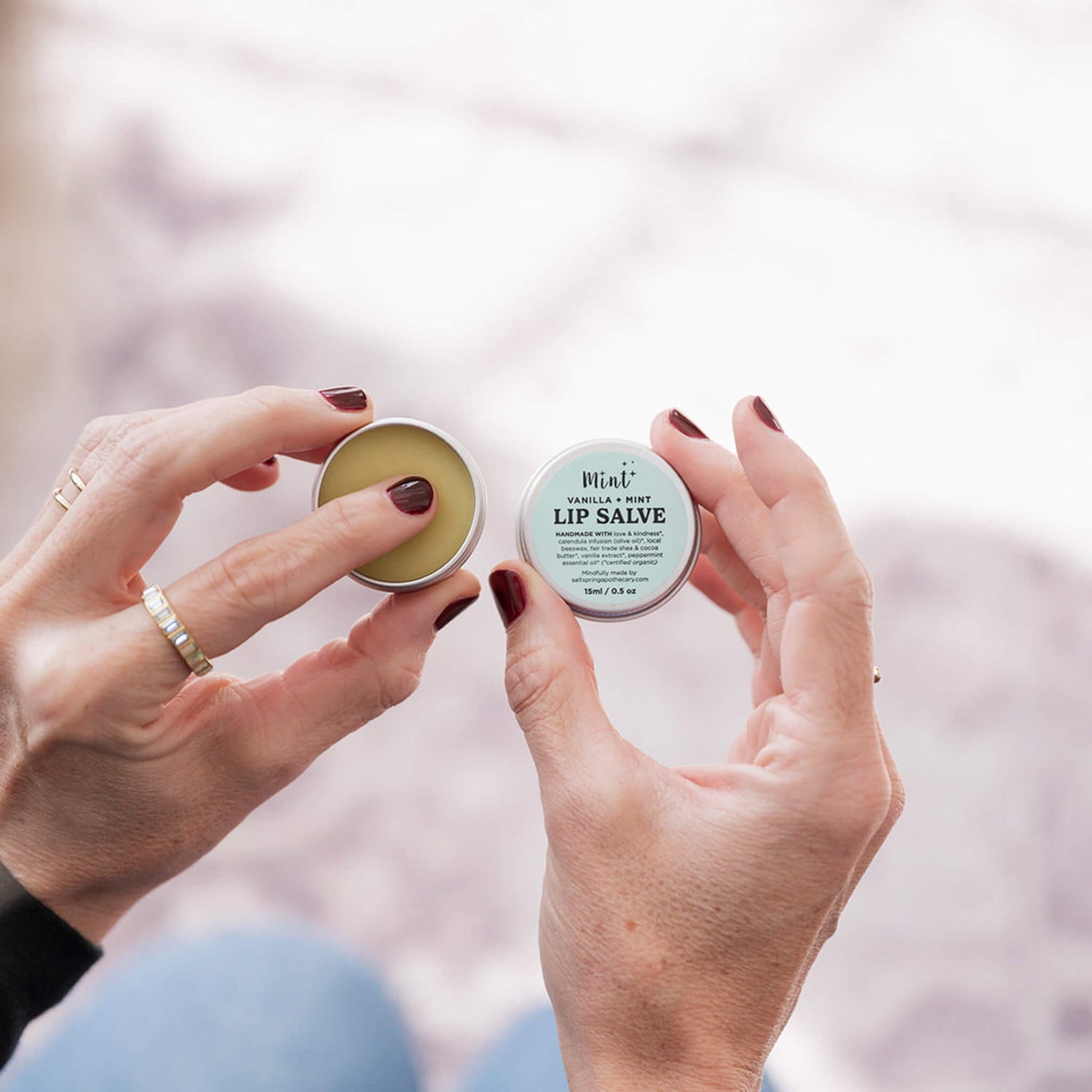 Two hands holding lip salve container with a blurred background
