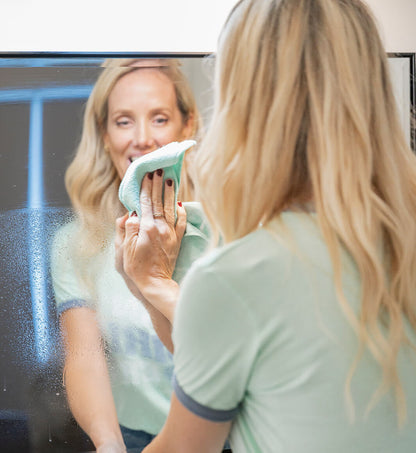 Woman cleaning a bathroom mirror with a green cloth.