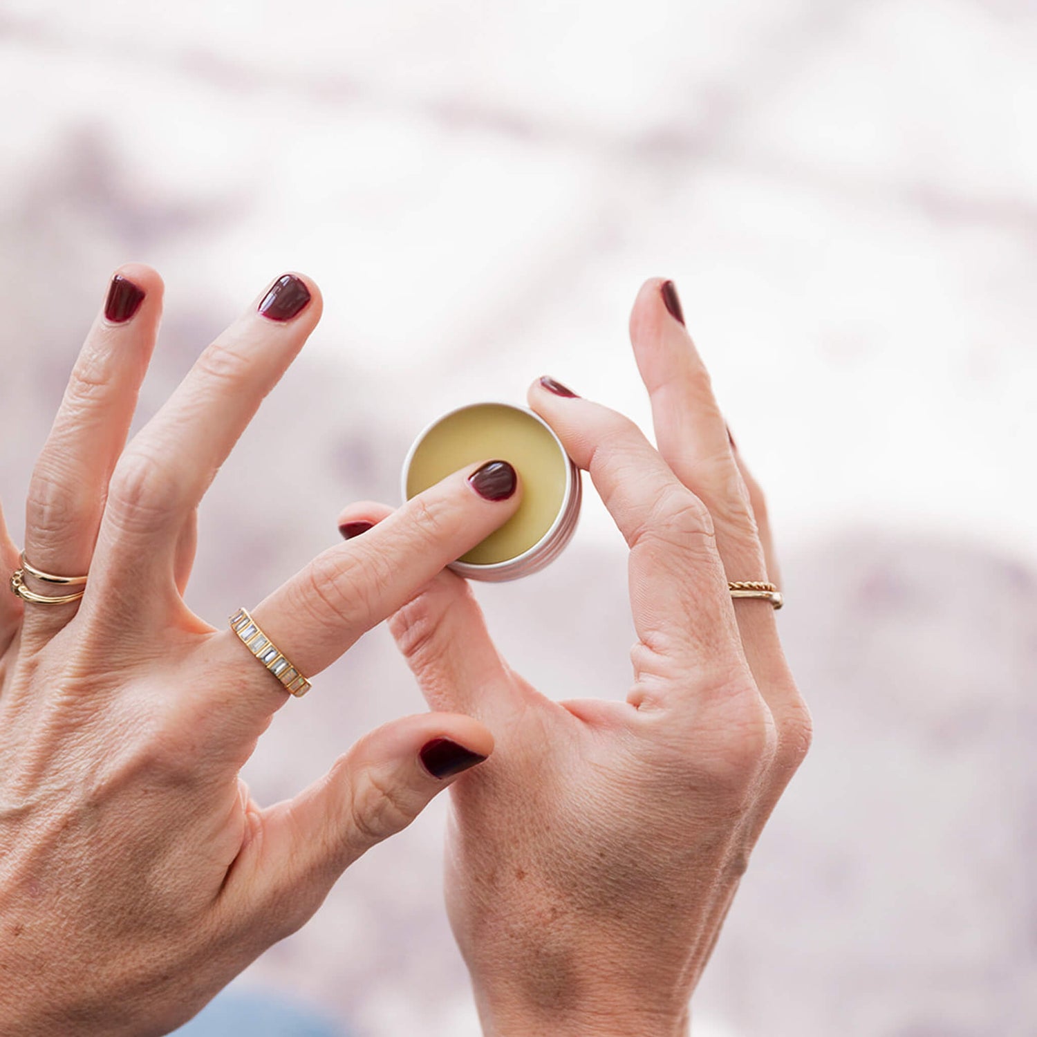 Close-up of hands holding a small round container with a white lid against a blurred background