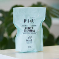 Mint Shower Steamers refill bag standing on a table with a natural green plant in the background, emphasizing the product’s eco-friendly packaging.