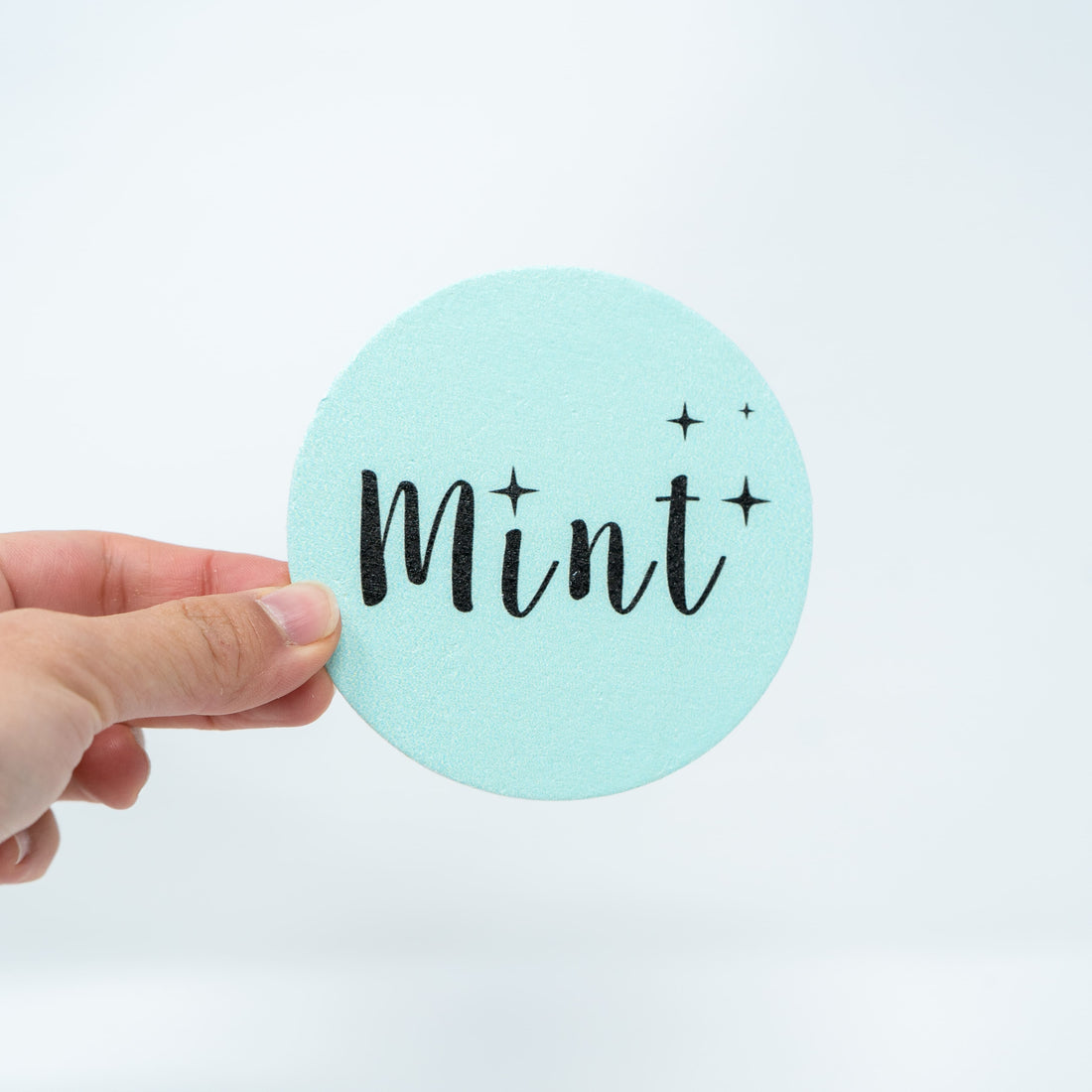 A close-up of the blue "Mint" sponge held by a hand, displayed against a plain white background, highlighting the sponge&