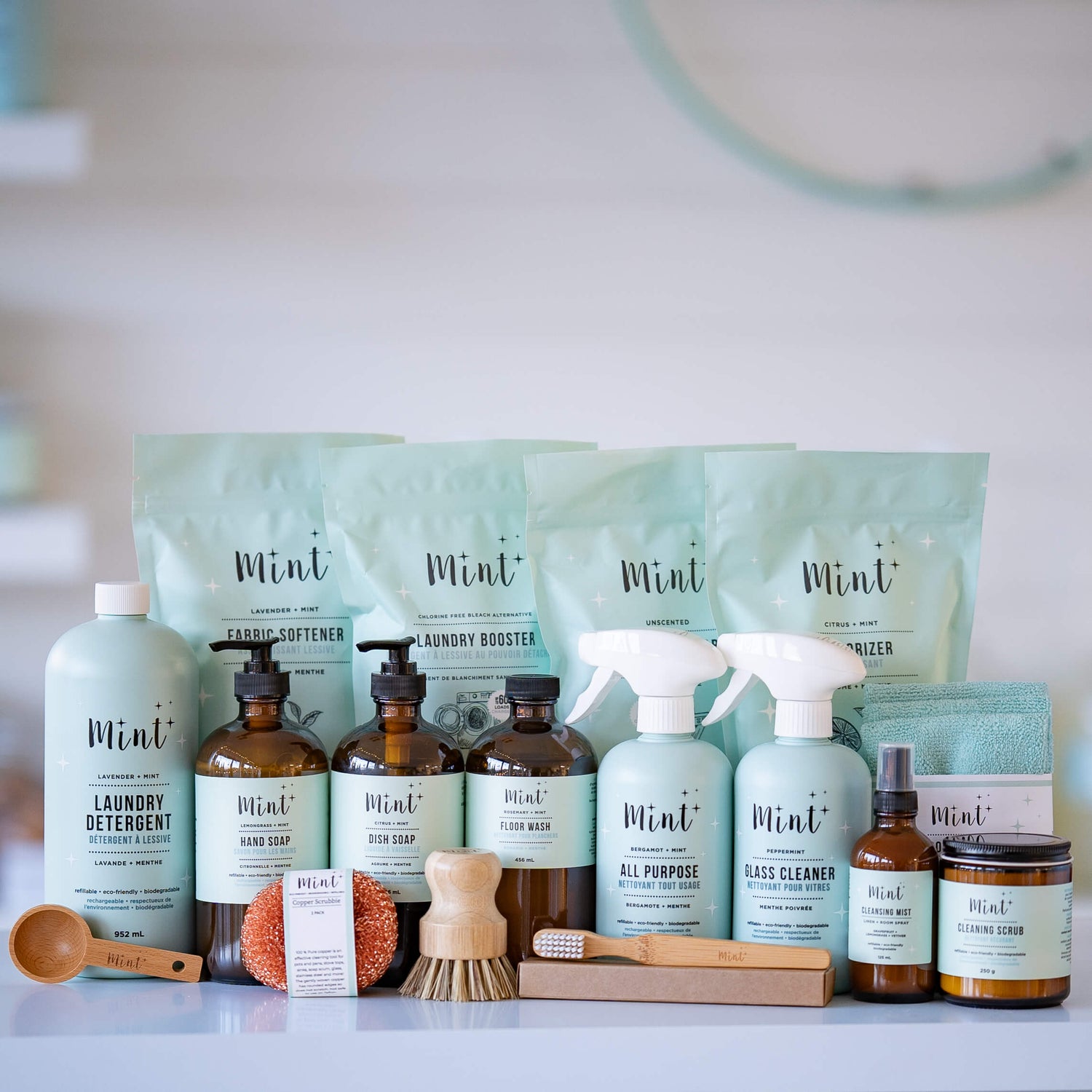 A variety of Mint Cleaning Products displayed on a white surface, featuring eco-friendly soaps, cleaners, laundry items, and accessories in light blue and earthy packaging.