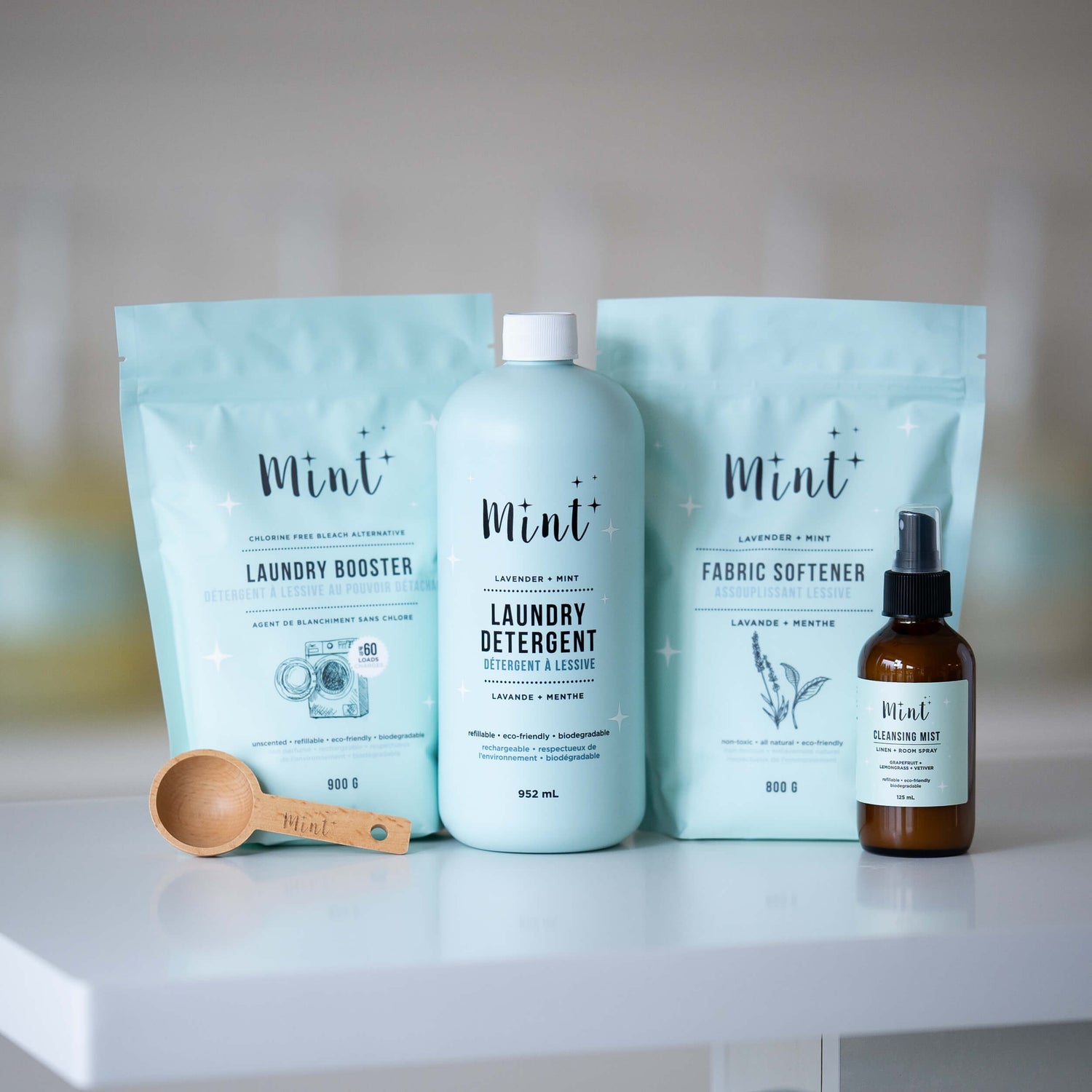 The Laundry Bundle by Mint Cleaning Products, featuring laundry detergent, fabric softener, laundry booster, cleansing mist, and a wooden scoop, displayed on a clean surface.