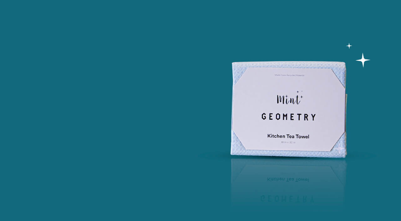 A Mint + Geometry Kitchen Tea Towel in light blue, neatly folded with its minimalist packaging. The background is deep teal, and the heading above reads 'Wipe, Dry, Repeat' with small sparkles for a clean and fresh feel."