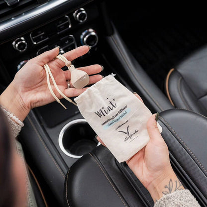Person holding a car air freshener and packaging inside a car.