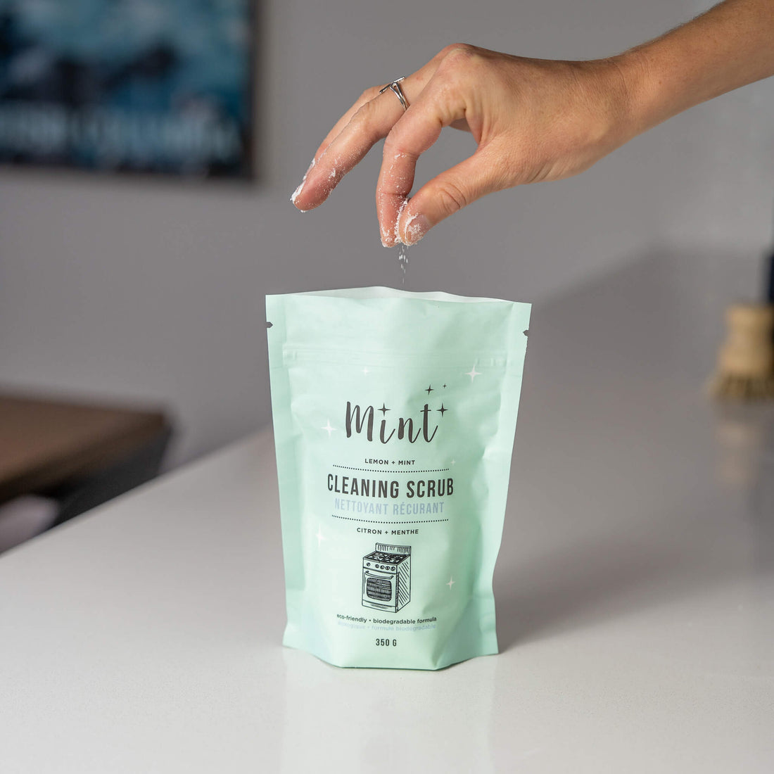 Hand holding a mint cleaning scrub packet on a neutral background