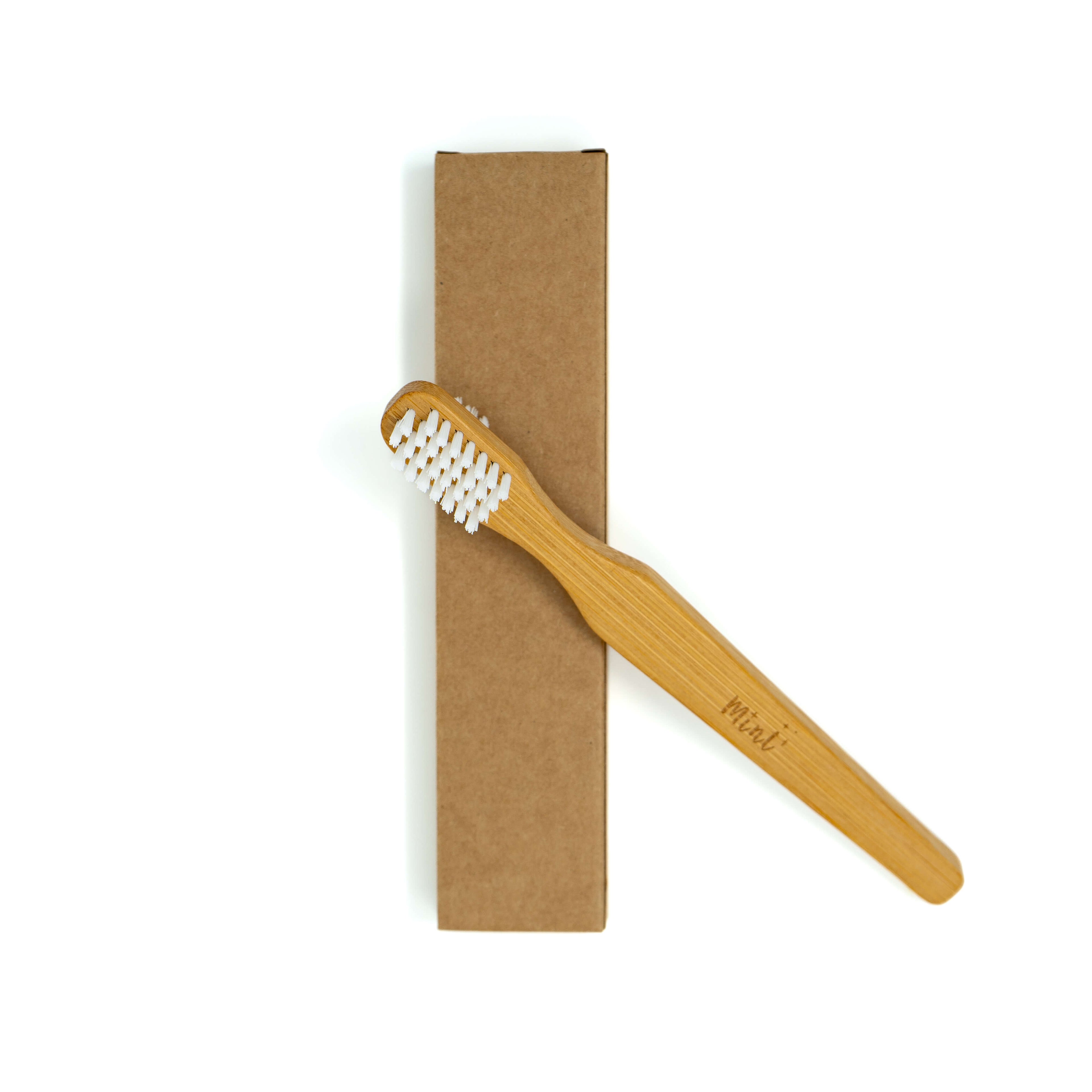 A Mint bamboo toothbrush with white bristles, engraved with the Mint logo, displayed alongside a recyclable kraft box on a white background