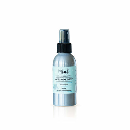 A silver aluminum spray bottle of Mint Outdoor Mist sitting on a wooden railing with a blurred green forest background. The label indicates it’s a 125 mL outdoor body spray that is DEET-free and plant-based.
